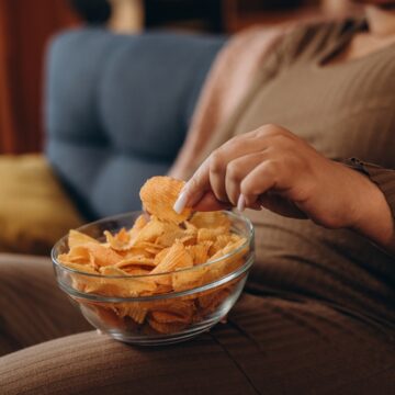A Person Sitting On A Couch And Eating Spicy Potato Chips From A Clear Glass Bowl A Person Sitting On A Couch And Eating Spicy Potato Chips From A Clear Glass Bowl