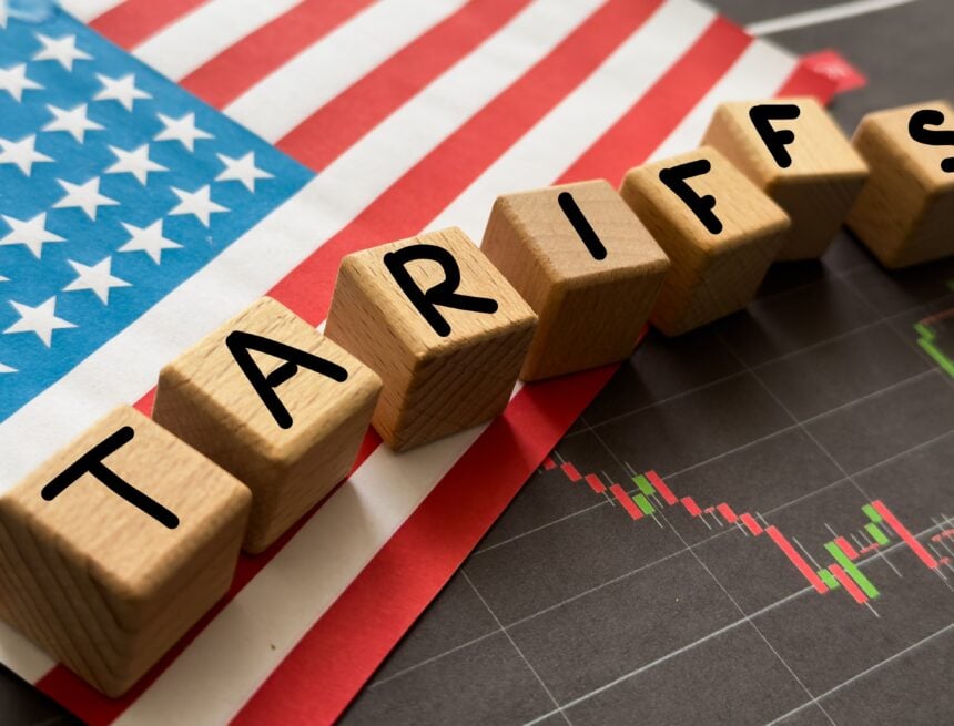 Wooden blocks spelling out the word "Tariffs" sitting atop a U.S. flag and a line graph with a downward red line.