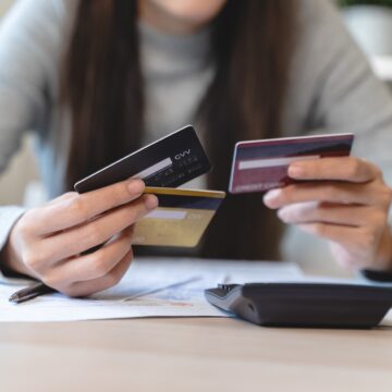 An image of a woman sitting at a table holding multiple credit cards.