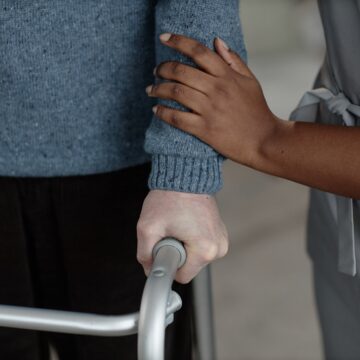 Cropped photo of a caregiver providing support to an older individual using a walker for mobility.