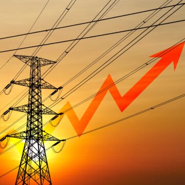 Conceptual image of high-tension power lines at sunset with a big, red upward-trending arrow in the background.