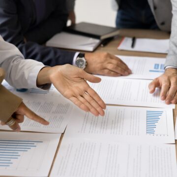 A close up of a group of businesspeople looking over documents, bar charts, and pie graphs spread across a table.