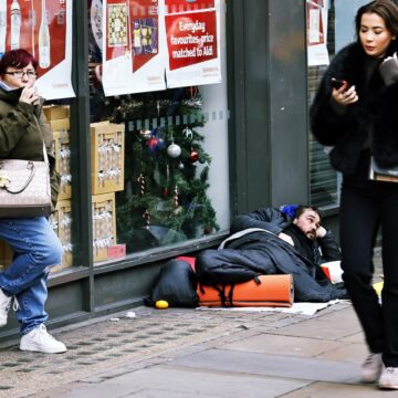 A Photo Of The Strand In London, UK, Featuring A Homeless Man Sleeping On The Street Outside A Sainsbury's Supermarket.