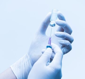 A close up of a latex-gloved medical professional preparing a syringe, likely for a vaccine or medication injection.