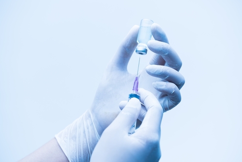 A close up of a latex-gloved medical professional preparing a syringe, likely for a vaccine or medication injection.