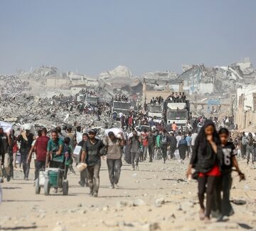 Displaced Palestinian civilians carry flour and food aid on a debris-strewn road amidst extensively damaged buildings in the Gaza Strip.
