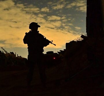 A silhouette of a soldier against a dusky sky likely during a night operation within a conflict zone such as Gaza.