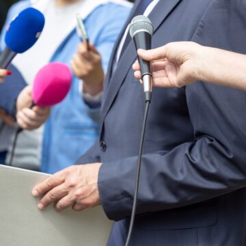 Image of a press conference or media event with journalists holding microphones. Image of a press conference or media event with journalists holding microphones.