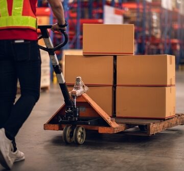 A factory worker pushing a loaded hand pallet truck in a warehouse or distribution center. A factory worker pushing a loaded hand pallet truck in a warehouse or distribution center.