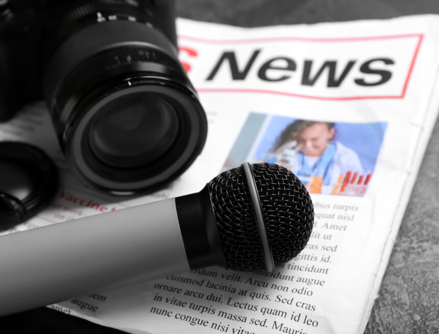 An image of the essential tools used in journalism, featuring a microphone resting on a newspaper alongside a camera. An image of the essential tools used in journalism, featuring a microphone resting on a newspaper alongside a camera.
