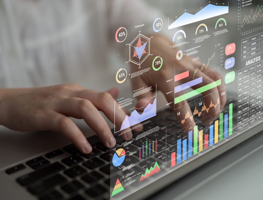 A futuristic heads-up data analytics display superimposed over a person typing on a laptop showing financial metrics, stock ticker, colorful charts, graphs, and percentage indicators for monitoring business performance. A futuristic heads-up data analytics display superimposed over a person typing on a laptop showing financial metrics, stock ticker, colorful charts, graphs, and percentage indicators for monitoring business performance.