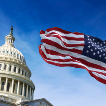 A photo of the U.S. Capitol Building dome with the American flag waving in the foreground.