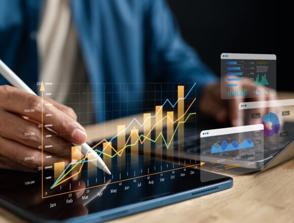 Image of a person analyzing a heads-up type display of financial charts and investment graphs on a tablet screen using a stylus to interact with digital graphs and charts displayed on the tablet.