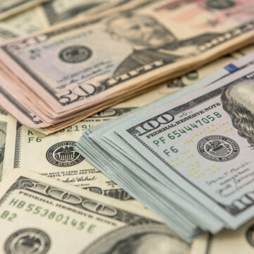 An image of a pile of assorted U.S. currency banknotes with prominent $100 notes and also a stack of $50 notes in the background.