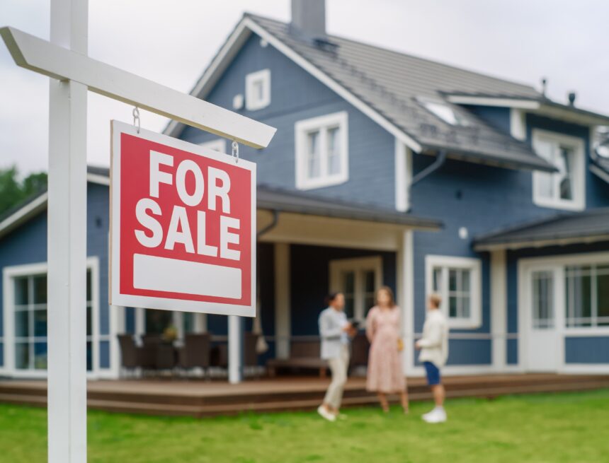 A young couple visiting a potential new home with a "For Sale" sign in the front yard.