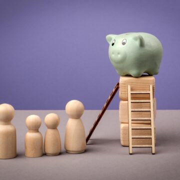 A Green Piggy Bank Sits Atop Stacked Wooden Blocks, Symbolizing A Goal Or Accumulated Savings, And A Small Ladder And Ramp Leading Up To The Piggy Bank, Suggesting A Path To Reach The Savings.