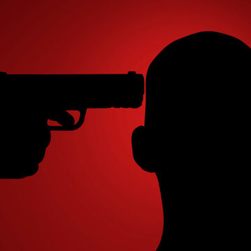 Silhouette Of A Man With A Gun Pointing At His Head Against A Dark Red Background.