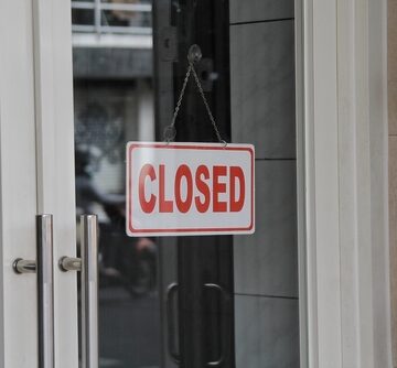 A "Closed" sign hanging on a store door indicating either a permanent closure, or closed for the day.