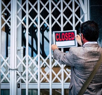 A business owner hanging a sign that reads "CLOSED" on a security gate of a store indicating a permanent closure.