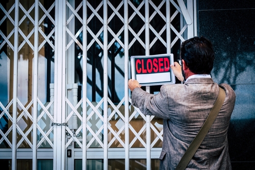 A business owner hanging a sign that reads "CLOSED" on a security gate of a store indicating a permanent closure.