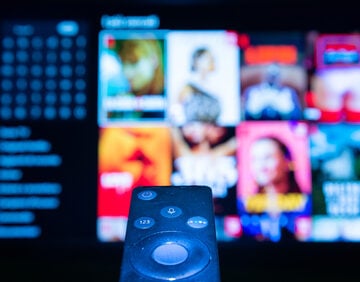 This image shows a remote control navigating a smart TV streaming interface, filled with blurred images of programming.