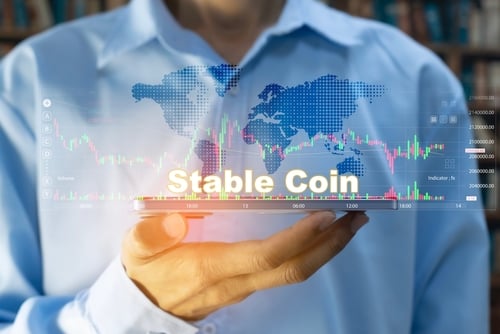 Businessman holding a tablet with the words "Stable Coin" floating amid various charts and graphs.
