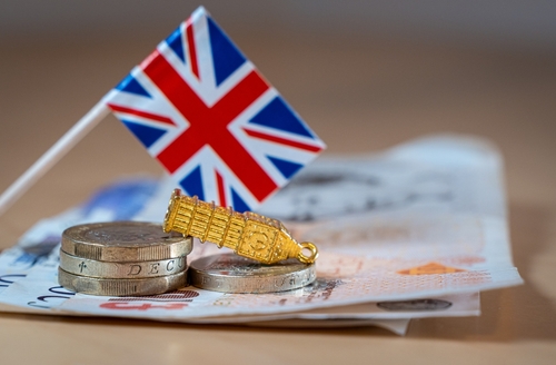 United Kingdom flag, British pound banknotes, coins, alongside a tipped-over miniature model of Big Ben.