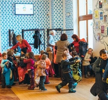 Preschool children grabbing coats and bags surrounded by teachers and assistants