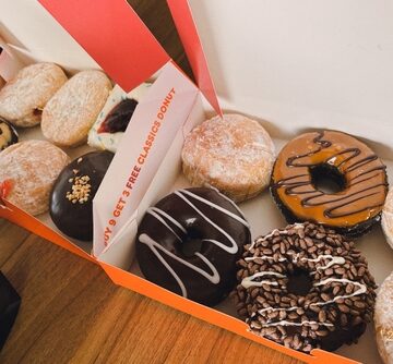 A box of Dunkin' Donuts containing a mix of classic and flavored varieties, including powdered sugar, chocolate-frosted, and sprinkle-topped doughnuts. A box of Dunkin' Donuts containing a mix of classic and flavored varieties, including powdered sugar, chocolate-frosted, and sprinkle-topped doughnuts.