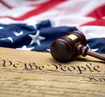 A draped American flag with a Judge's gavel and a copy of the Constitution. A draped American flag with a Judge's gavel and a copy of the Constitution.