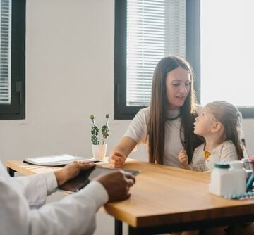 A pediatrician holding a tablet meets with a mother and her young child