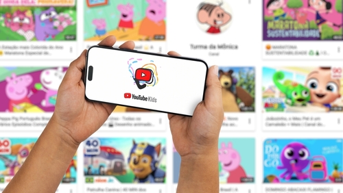 A child holding a smartphone displaying the YouTube Kids app, which is a dedicated video platform developed by Google specifically for children.