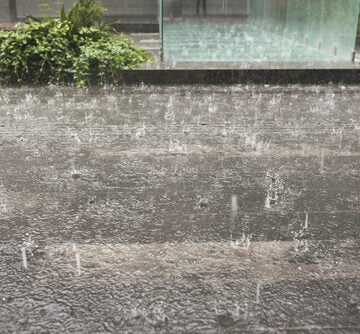A close-up view of raindrops hitting a dark, textured pavement