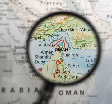 A view through a magnifying glass of a map showing the Musandam Peninsula, a strategically vital exclave of Oman that juts into the critical maritime chokepoint of the Strait of Hormuz.