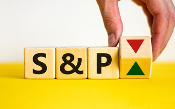 Wooden cubes displaying "S&P" next to a hand is turning over cube with red and green arrows, symbolizing market fluctuations.