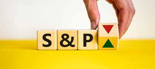 Wooden cubes displaying "S&P" next to a hand is turning over cube with red and green arrows, symbolizing market fluctuations.