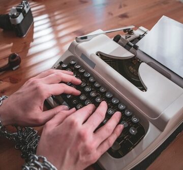 An image of a person handcuffed to a vintage typewriter, suggesting the concept of censorship.