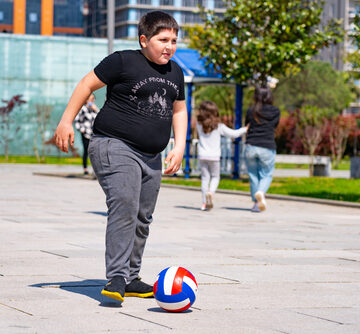 A heavy-set child playing with a volleyball in a public outdoor area.