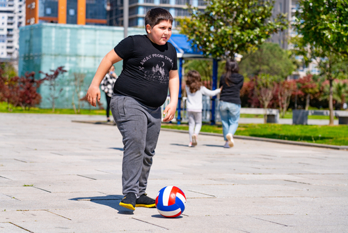 A heavy-set child playing with a volleyball in a public outdoor area.