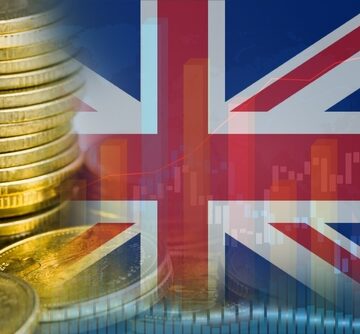 A stack of coins alongside a financial trading chart and rhe backdrop is the flag of the United Kingdom, commonly known as the Union Jack.