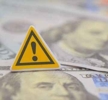 A yellow warning sign on top of cash, symbolizing a financial alert.