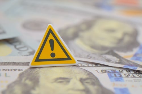A yellow warning sign on top of cash, symbolizing a financial alert.