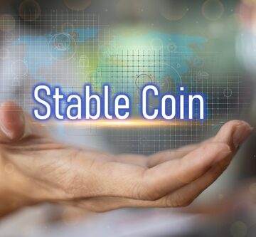 The image displays a hand holding the text "Stable Coin" overlaid on a blurred graphic representing digital finance.