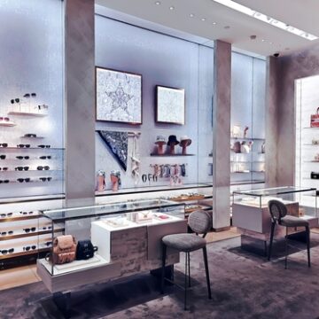 The image displays the interior of a Dior luxury boutique, showcasing leather goods, accessories, and eyewear.