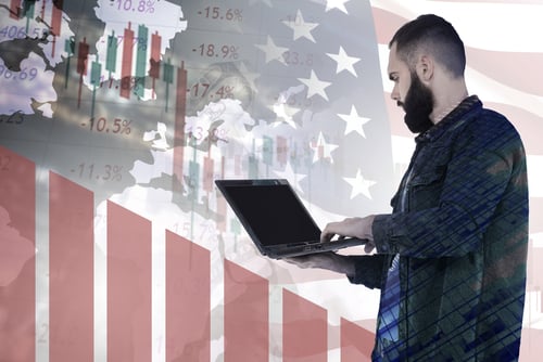 Concept image of economic fluctuations in the U.S., featuring a man analyzing financial trends on a laptop against a background of the American flag and declining stock graphs.