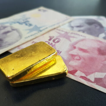 Gold bars rest on top of Turkish Lira banknotes, specifically the 10 Lira note featuring Mustafa Kemal Atatürk.
