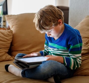 A young person intently using a tablet computer while relaxing on a couch.
