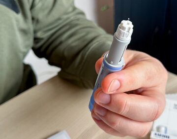 A person holding a pre-filled injection pen, such as those used for Ozempic or Wegovy to treat type 2 diabetes or for weight management.