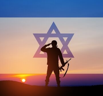 A silhouette of a soldier salutes against a sunset in the desert and the flag of Israel.