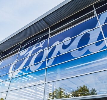 A modern Ford dealership building with glass walls and a large Ford logo.